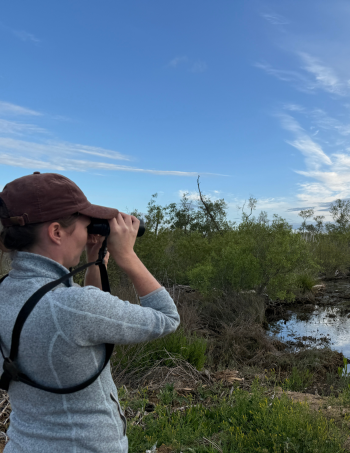 A woman looks through binoculars in the wetlands.
