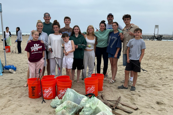 People at the beach surrounded by tools, buckets, and bags of trash.