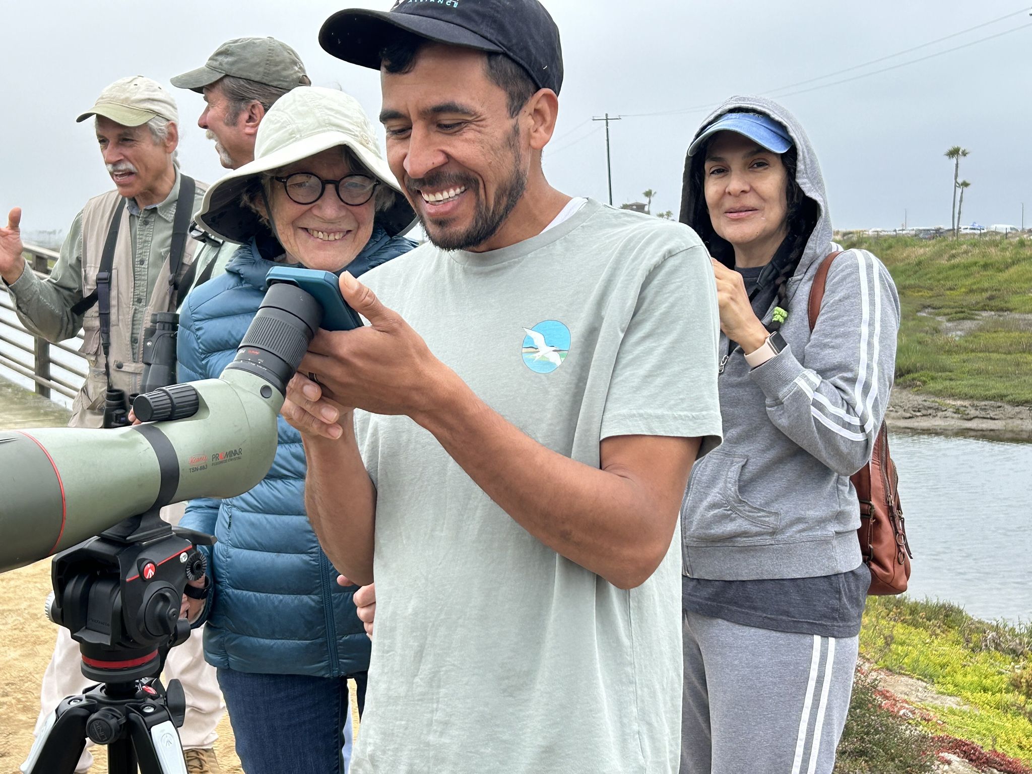 A man stands at a scope looking for birds with others in the background.