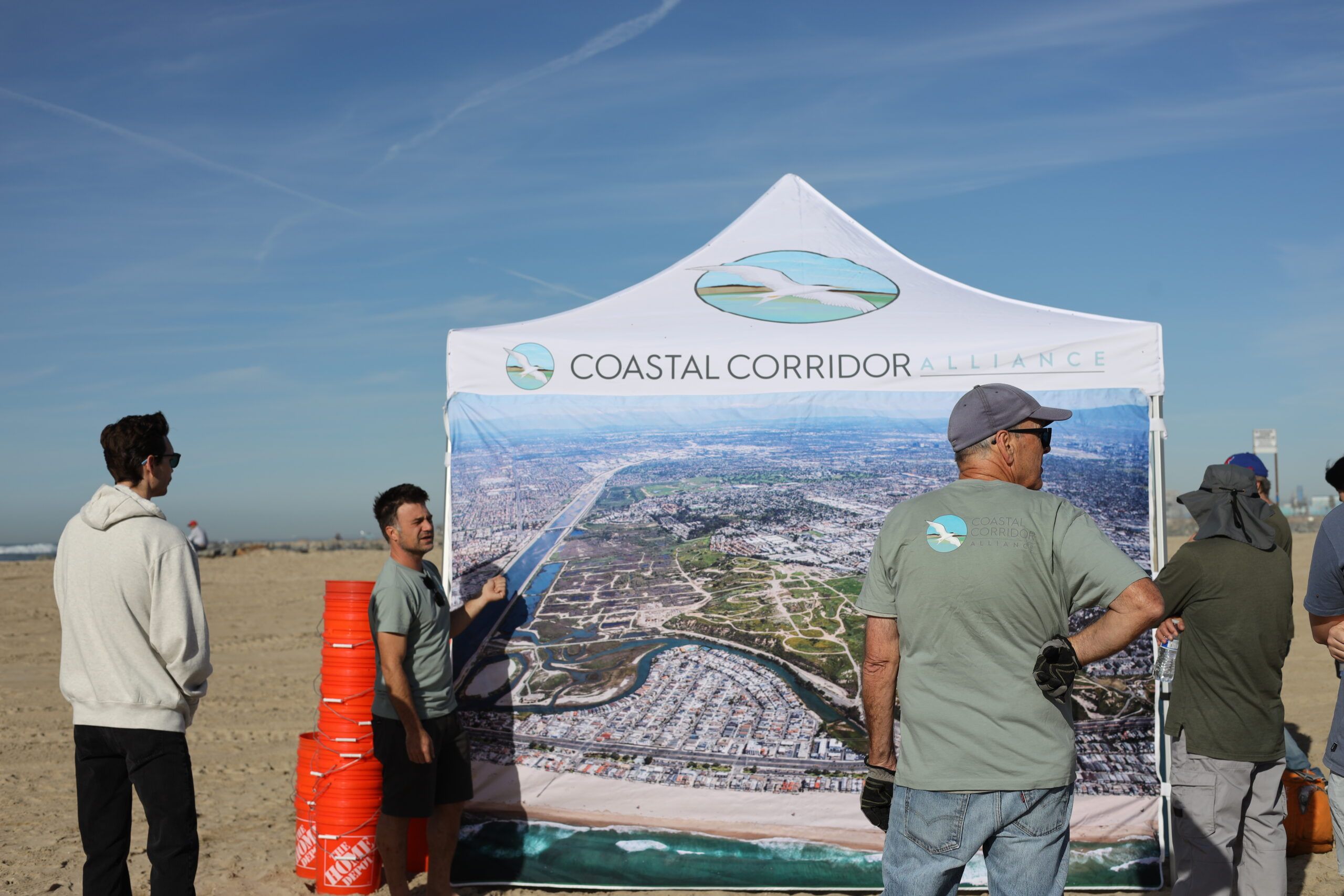 People at an event near a canopy ready to clean trash off the sand.