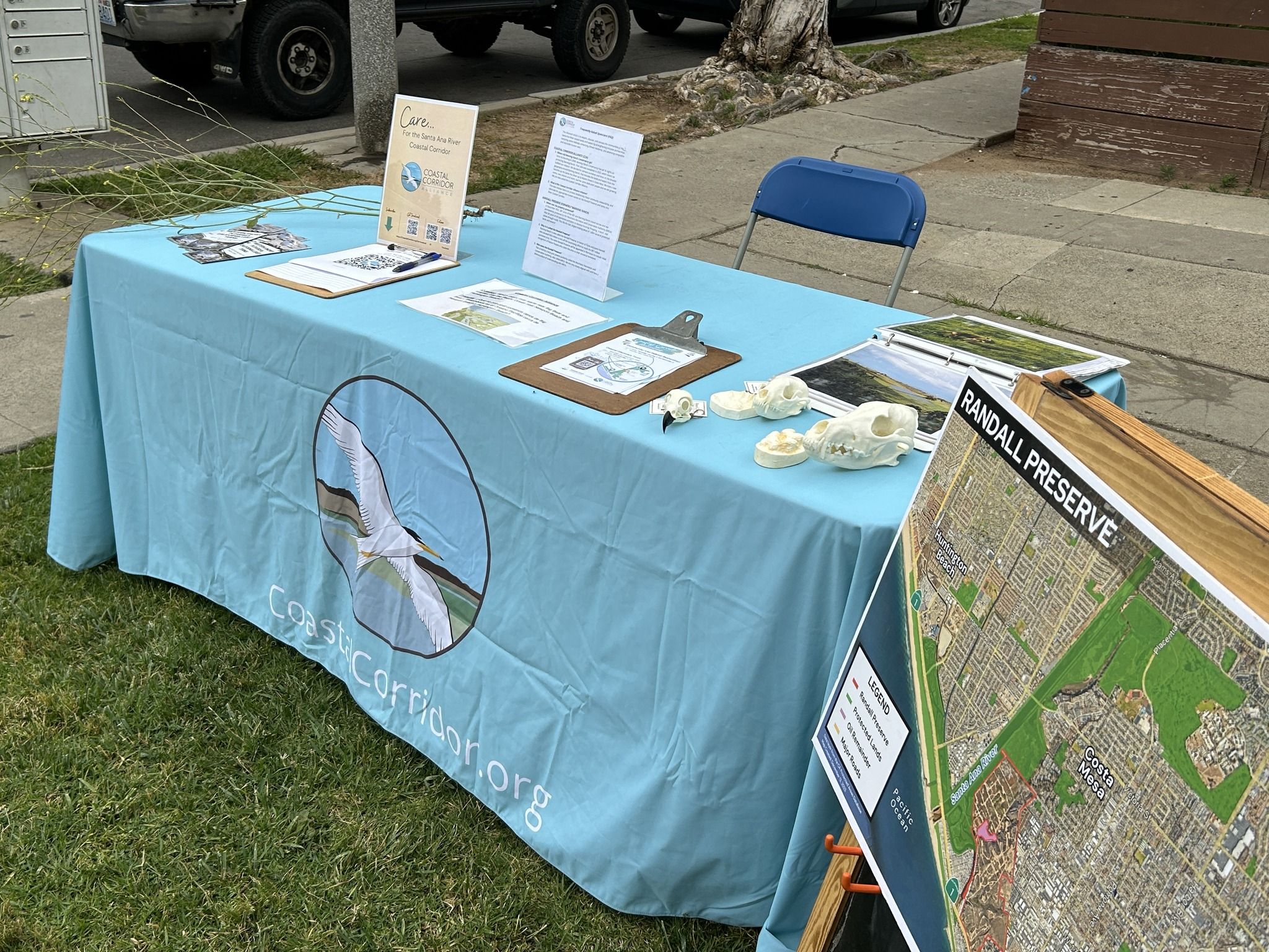 An image of a table with a blue table cloth various items on the table and map to its right. It is an outdoor setting with cars in the background.